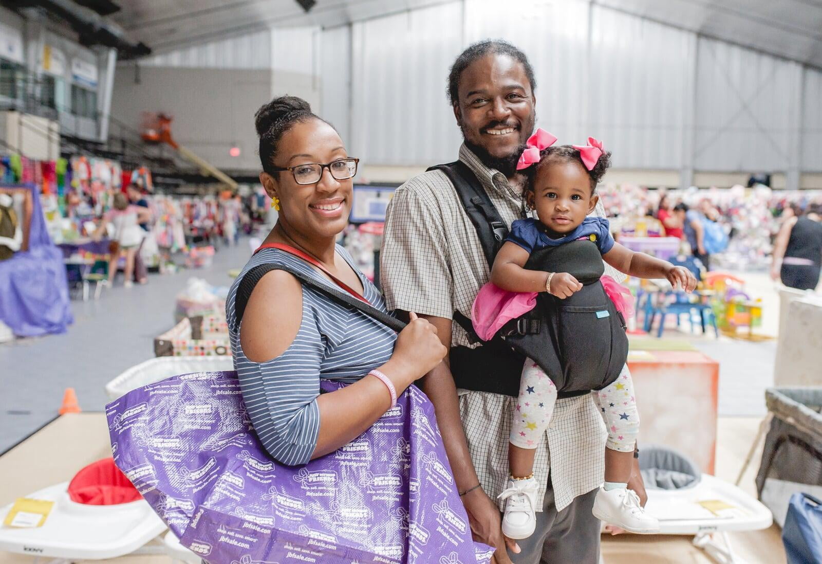 Wife holding purple shopping bag, husband and toddler girl in carrier shopping