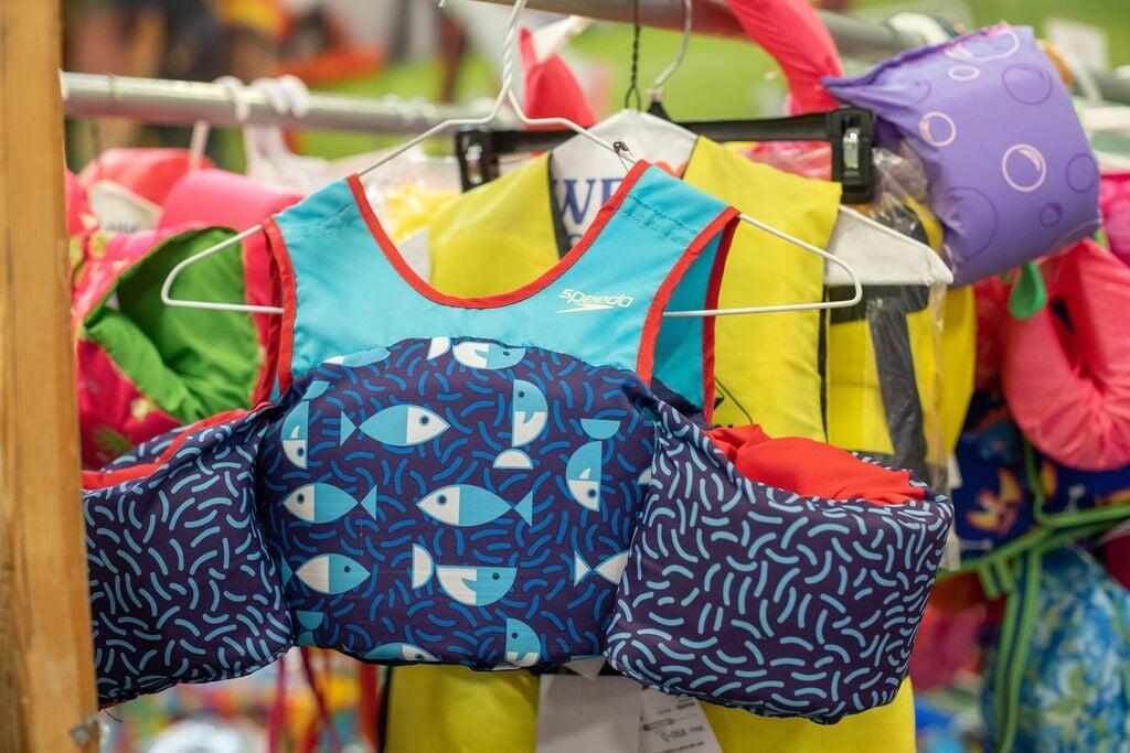 A mom and dad shopping at the JBF sale. Mom is holding a purple JBF shopping bag and dad carries his daughter in a front-pack carrier.