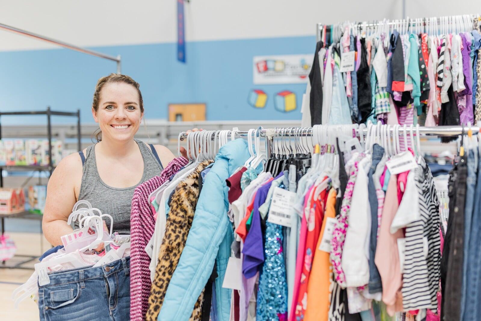 A JBF Team Member wears a black JBF apron while organizing infant clothing on the clothing racks.